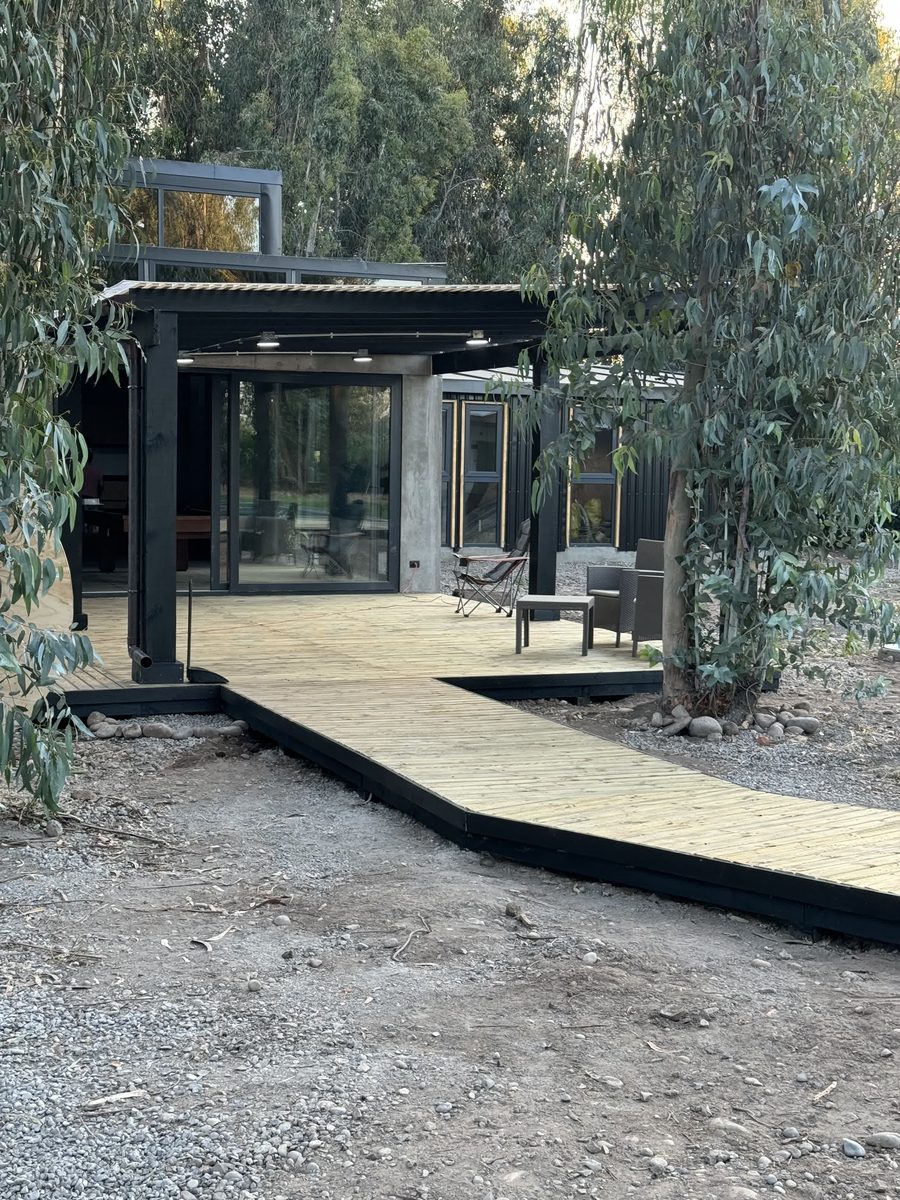Deck de madera que rodea una casa de estructura negra entre árboles