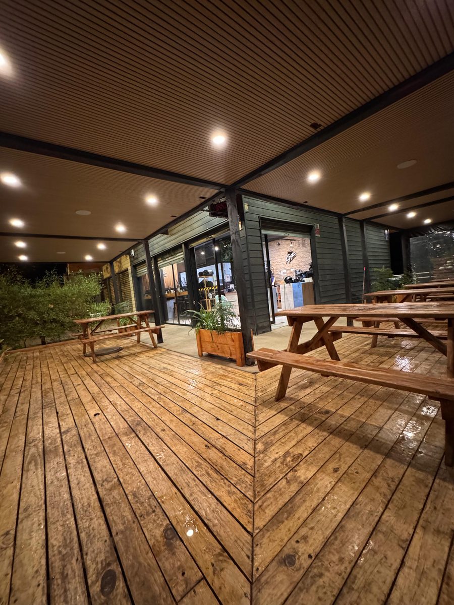 Deck de madera de noche bajo una techumbre con cielo de wall panel y focos LED