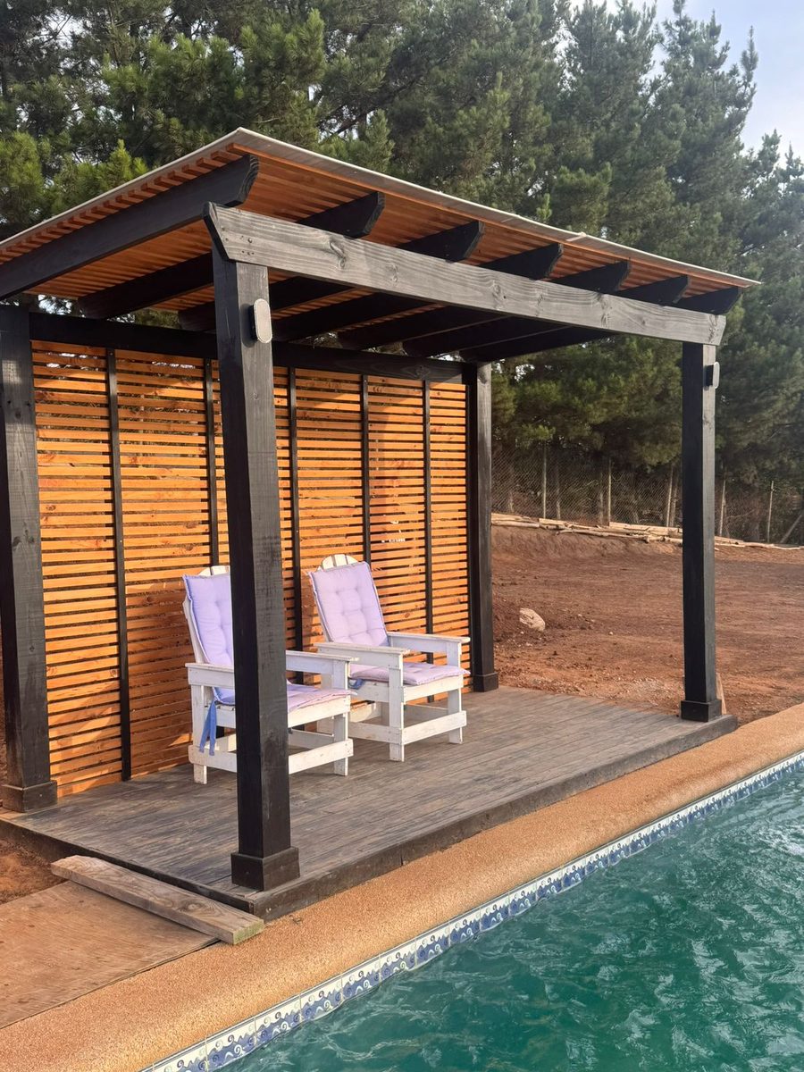Pérgola con piso de terraza y cortavista de listones junto a una piscina