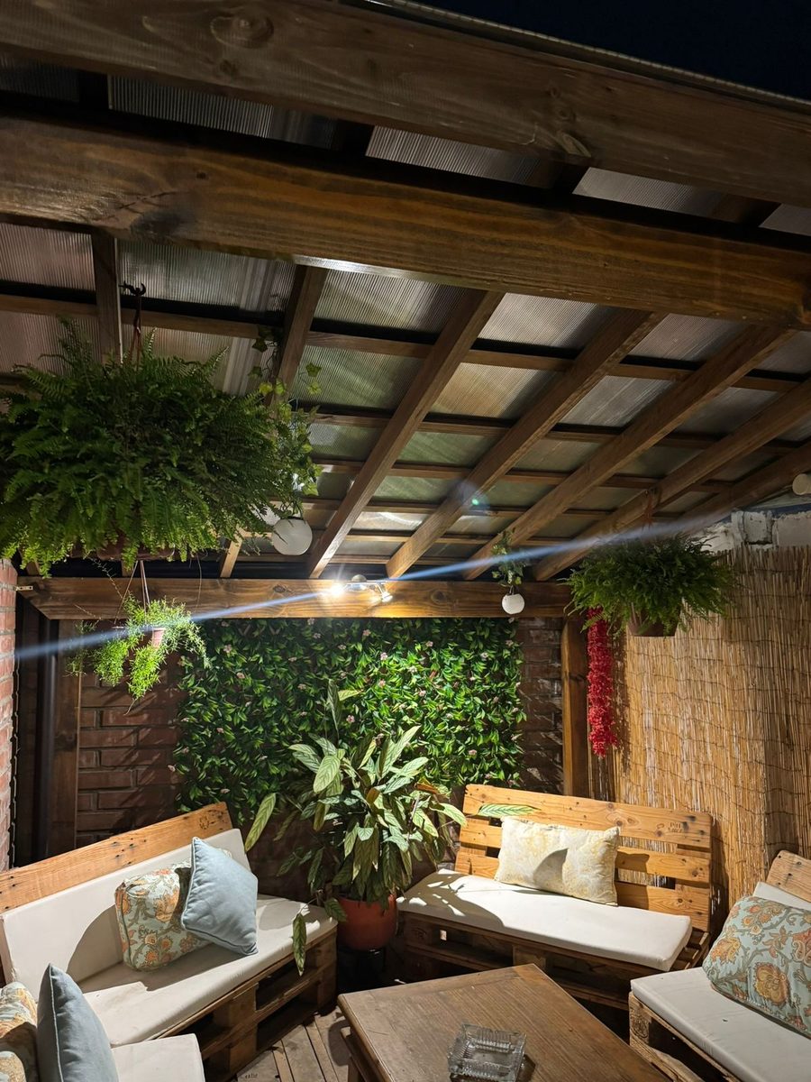 Terraza techada de noche con muebles de palets, muro verde e iluminación cálida