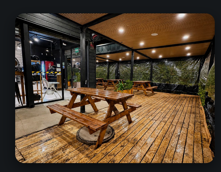 Terraza techada con deck de madera, cielo de listones, iluminación empotrada y cortinas transparentes